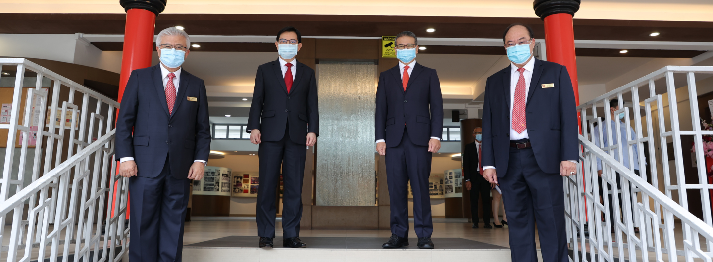 Four men in suits and face masks stand on a landing with white railings.